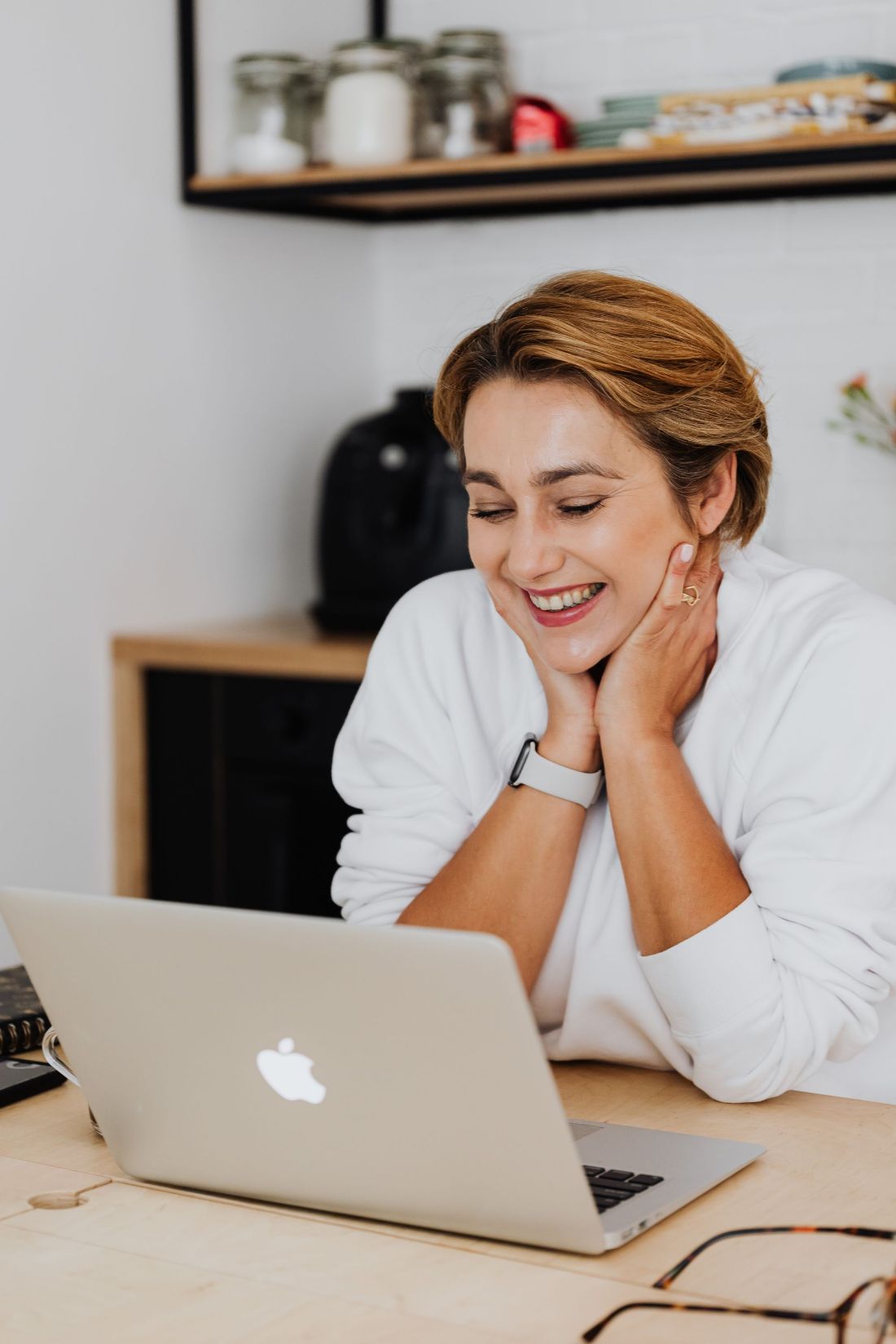 A woman laughing at her laptop in her kitchen